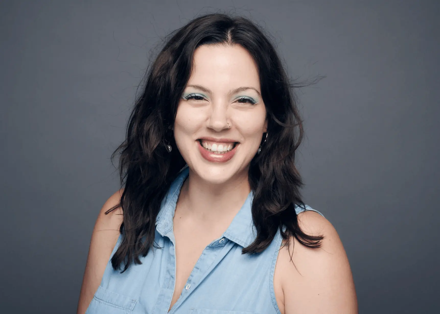 Smiling woman with wavy hair and blue eyeshadow.