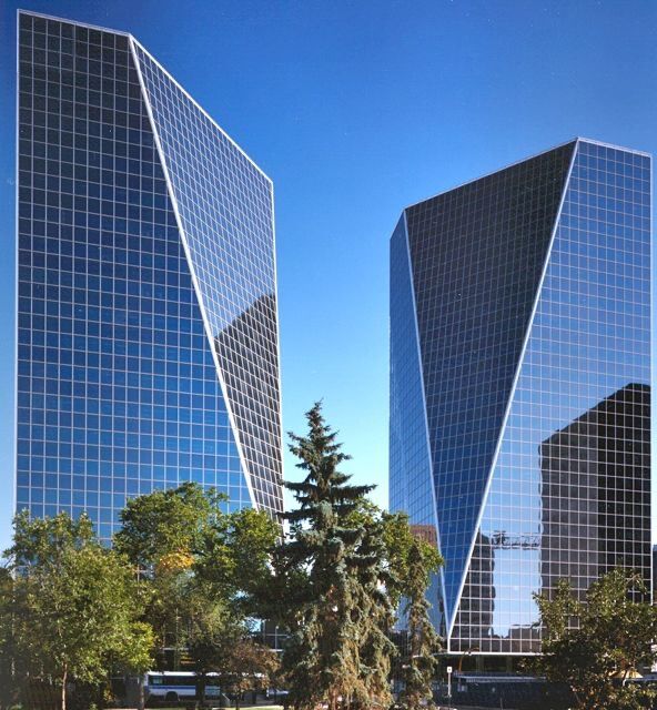 Two modern glass skyscrapers with trees in foreground.